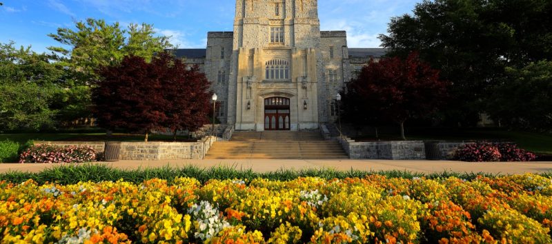 Burruss Hall in May with a clear sky and flowers in front of the building.